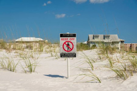 Photo for Protected Area Keep Off signpost on a white sand dunes at Destin, Florida. Signpost at the center of the sand dunes near the residential area against the blue sky at the back. - Royalty Free Image