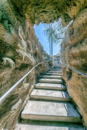 Photo for San Antonio, Texas- Narrow staircase in a manmade cave with wall-mounted handrails. Pathway heading outside with leafless trees and posts against the clear sky background. - Royalty Free Image