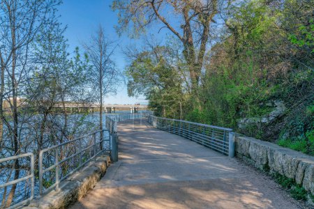 Austin, Texas- Boardwalk beside the mountain and river. Concrete bike path and pedestrian pathway with a view of the bridge over the river.