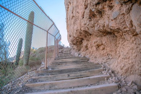Photo for Phoenix, Arizona- Manmade wooden steps on a mountainside hiking trail at Camelback Mountain. There is a chainlink fence on the left near the saguaro cactuses and a rocky mountain wall on the right. - Royalty Free Image