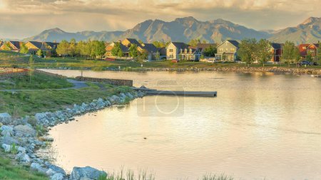 Photo for Panorama Panoramic view of the residential area against the mountain range background at Daybreak, Utah. Oquirrh lake waterfront with field and rocks near the shoreline and water with reflection of the sky. - Royalty Free Image