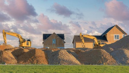 Photo for Panorama Puffy clouds at sunset Construction sand piles with two excavators at Utah. There is a lawn at the front of the construction sands and two unfinished two houses with asphalt shingle roofs and wooden cork wall insulation. - Royalty Free Image