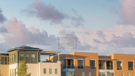 Téléchargez les photos : Panorama Nuages gonflés au coucher du soleil Extérieur des étages supérieurs de deux immeubles d'appartements complexes avec balcons. Il y a un bâtiment avec revêtement mural brun à gauche à côté de l'immeuble d'appartements avec des unités sur le toit. - en image libre de droit