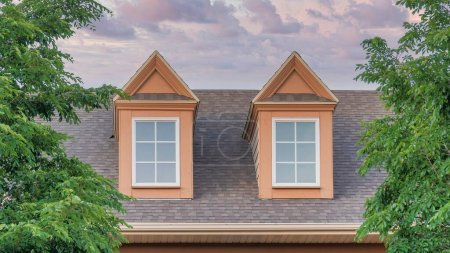 Photo for Panorama Puffy clouds at sunset Roof of a house with two gabled dormer windows at Utah. Roof exterior of a house with gray asphalt composite shingles and vinyl wood wall sidings with trees at the front. - Royalty Free Image