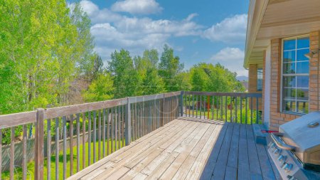 Photo for Panorama White puffy clouds Wooden deck of a house with stainless steel gas barbecue grill. Deck of a house with bricks and a view of a lawn and trees of a fenced backyard in Utah. - Royalty Free Image