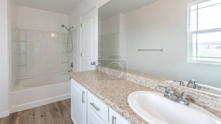 Traditionelles Badezimmer mit Waschbecken und Dusche Kombi-Set. Es gibt eine Badewanne mit Handbrause neben dem Waschbecken mit Granitplatte und Spiegel mit Spiegelung des Fensters.