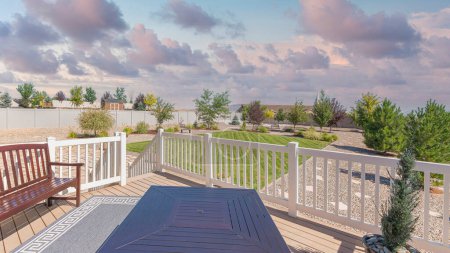Photo for Panorama Puffy clouds at sunset Deck of a house with potted pine tree near the fire pit table and bench with carpet in the middle. Lounge are of a fence house with large yard with trees and lawn against the neighborhood and sky. - Royalty Free Image