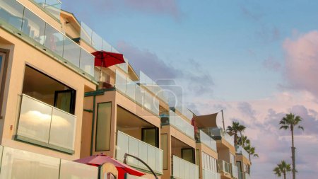 Foto de Panorama Nubes hinchadas al atardecer Edificio del hotel Beach house en una vista de bajo ángulo en Oceanside, California. Exterior de un edificio con sombrillas rojas al aire libre en los balcones con barandillas de cristal. - Imagen libre de derechos