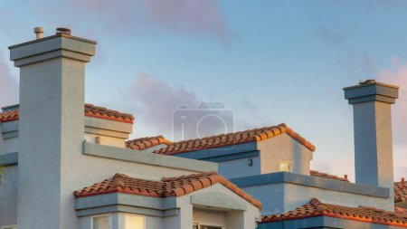 Foto de Panorama Nubes hinchadas al atardecer Edificio de estilo mediterráneo gris con techos de tejas de hormigón rojo en Oceanside, California. Exterior de un edificio con ventanas y balcones de cristal reflectante contra el cielo azul claro. - Imagen libre de derechos