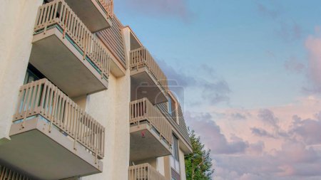 Téléchargez les photos : Panorama Nuages gonflés au coucher du soleil Vue à angle bas d'un immeuble à Oceanside, Californie. Extérieur d'un bâtiment avec balustrades sur les balcons sur le fond bleu ciel clair. - en image libre de droit