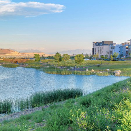 Photo for Square Panoramic view of the residential area against the mountain range background Daybreak, Utah. Oquirrh lake waterfront with field and rocks near the shoreline and water with reflection of the sky. - Royalty Free Image