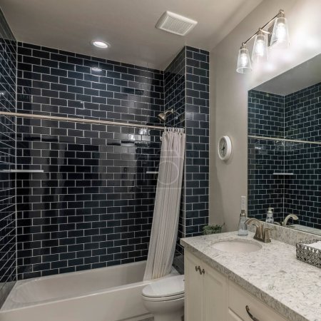 Square Master bathroom with double vanity sink and shower tub with black subway tiles surround. Interior of a bathroom with towels on a tray at the top of the granite counter near the wall mirror.