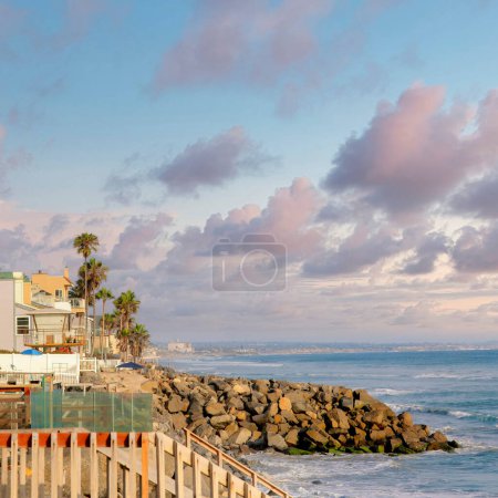 Foto de Square Nubes hinchadas al atardecer Fila de edificios de casas de playa frente al mar en Oceanside, California. Hay escaleras y palmeras cerca del malecón rocoso en la parte delantera de los edificios. - Imagen libre de derechos
