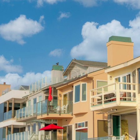 Foto de Square Nubes hinchadas blancas Fila de alojamientos en Oceanside, California. Edificio exterior con diferentes diseños y balcones con barandillas de cristal contra el cielo azul claro. - Imagen libre de derechos