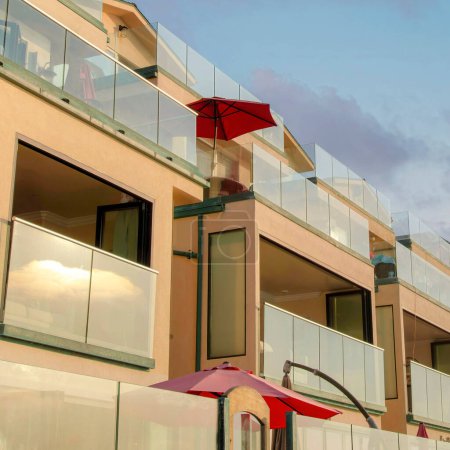 Foto de Square Nubes hinchadas al atardecer Edificio del hotel Beach house en una vista de bajo ángulo en Oceanside, California. Exterior de un edificio con sombrillas rojas al aire libre en los balcones con barandillas de cristal. - Imagen libre de derechos