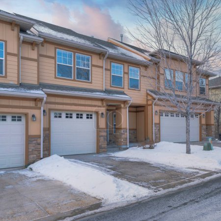 Photo for Square Puffy clouds at sunset Townhouses exterior with attached garage and a driveway cleared of snow. Two storey complex houses with stone bricks and wooden siding along the road with a view of the neighborhood. - Royalty Free Image