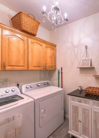 Photo for Vertical Craftsman laundry room with cabinets and hanging shelves. There are laundry machines on the right below the wall cabinets with woven basket on top across the wood planks wall with wreath on right. - Royalty Free Image