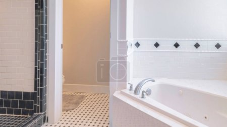 Foto de Panorama Amplio baño interior con azulejos blancos y negros. Hay un puesto de ducha sin puerta con adornos negros a la izquierda cerca del cuarto de baño y una bañera de esquina a la derecha cerca de la ventana con persianas. - Imagen libre de derechos