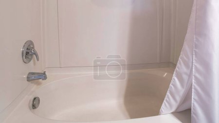 Foto de Panorama Kit combinado de bañera de ducha con panel de pared acrílico y cortina de ducha blanca. Bañera de ducha cerca de la pared marrón por encima del panel de pared y un grifo montado en la pared y la cabeza de ducha. - Imagen libre de derechos