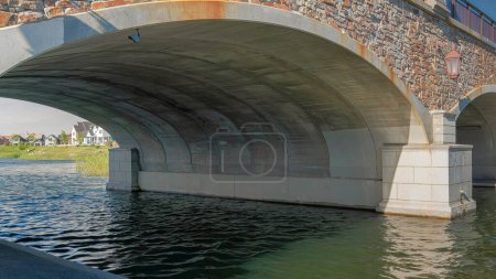 Photo for Panorama Whispy white clouds Double arched bridge with stone walls and railings over the Oquirrh Lake at Daybreak, Utah. There are wall lamps on the stone walls of the bridge with concrete path on either side of the lake. - Royalty Free Image