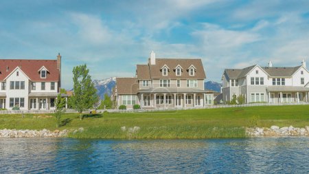 Photo for Panorama Whispy white clouds Oquirrh Lake waterfront at Daybreak, Utah residential area. Reflective water of the lake against the large home facades against the mountains and clear blue sky. - Royalty Free Image
