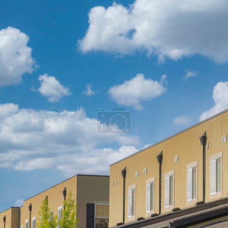 Foto de Square Nubes hinchadas blancas Modernas casas adosadas con canalones de lluvia al amanecer, Utah. Vista de ángulo bajo del edificio complejo con revestimiento de hormigón verde amarillo claro y ventanas correderas de vidrio. - Imagen libre de derechos