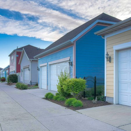 Photo for Square Whispy white clouds Exterior of garages across each other in a residential area at Daybreak, Utah. There is a concrete road in the middle of the garages with white sectional garage doors. - Royalty Free Image