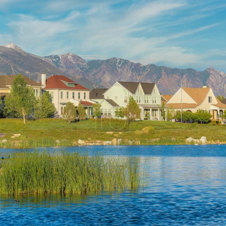 Photo for Square Whispy white clouds Oquirrh Lake with curved asphalt walkway on the side at Daybreak, Utah. There are houses with different designs and structures against the mountains with snow at the background. - Royalty Free Image