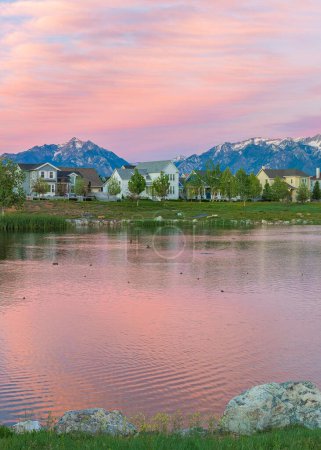 Photo for Vertical Reflective Oquirrh Lake waterfront Daybreak, Utah. Panoramic view of the lake at the front of the houses and fields against the mountain range and sky with pink hue. - Royalty Free Image