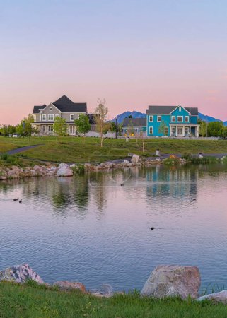 Photo for Vertical Reflective Oquirrh Lake waterfront at Daybreak, Utah. Panoramic view of the lake at the front of the houses and fields against the mountain range and sky with pink hue. - Royalty Free Image