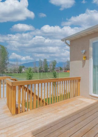 Photo for Vertical White puffy clouds Wooden deck of a fenced house with sliding glass door. House deck with a view of a neighborhood houses and a road with a passing vehicles against the view of a mountain range at the back. - Royalty Free Image