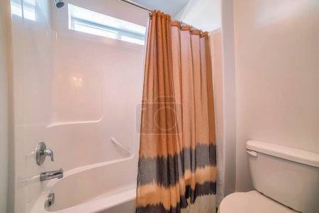 Téléchargez les photos : Salle de bain traditionnelle avec rideau de douche brun à rayures noires. Il y a une toilette à droite près de la baignoire de douche avec panneau mural en acrylique et pomme de douche et robinet en acier inoxydable. - en image libre de droit