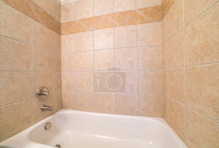Baignoire en alcôve close up avec carreaux de céramique marron entourent. Intérieur de la salle de bains avec robinet mural en acier inoxydable et pomme de douche.