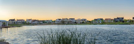 Photo for View of Oquirrh Lake at the front of residential buildings at Daybreak, Utah. There is a covered dock on the left side at the front of large houses against the sunset sky horizon at the background. - Royalty Free Image