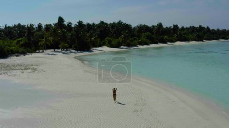 Foto de Feliz chica alegre saltando en la playa de arena de agua en Maldivas tropicales exóticas. Sonriente dama alegre divirtiéndose en la playa, disfrutando del sol y el agua cristalina. - Imagen libre de derechos