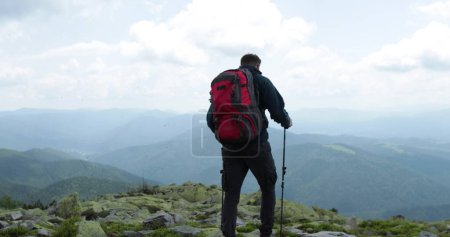 Foto de Un viaje en las montañas, un turista va con una mochila y palos, viaja a través del terreno rocoso de las altas montañas, excursionistas independientes y solitarios en las rocas. - Imagen libre de derechos