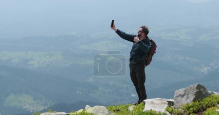 Foto de Un viajero en la cima de una montaña está hablando por teléfono, tomando fotos y teniendo un video chat. Concepto de comunicación en lugares remotos del mundo. - Imagen libre de derechos