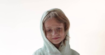 Foto de Un chico pequeño y guapo. Retrato de cerca. Un chico con el pelo largo en una capucha, posando en el estudio. - Imagen libre de derechos