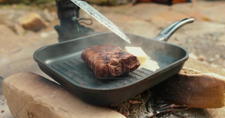 Photo for Adding butter to a steak on a hot pan in the process of grilling meat outdoors. Cooking meat on an open fire in nature on a tourist trip. - Royalty Free Image
