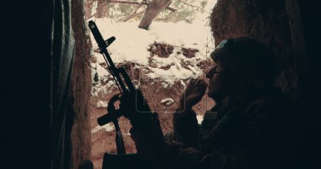 Foto de Un soldado anciano se sienta con una ametralladora en una trinchera, dugout y fuma. Acciones militares en el este de Ucrania 2023. Guerra ruso-ucraniana. - Imagen libre de derechos