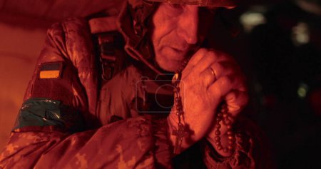 Foto de Retrato cinematográfico de cerca de un viejo soldado orando con esperanza mientras estaba sentado en un foso. Rezando con un rosario en uniforme militar de camuflaje, esperando paz y libertad - Imagen libre de derechos