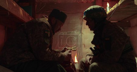 Foto de Confesión de un soldado ucraniano en un oscuro foso. El capellán y el alcaide se sientan uno frente al otro y hablan. - Imagen libre de derechos