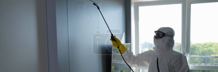 Desinfektion zur Vernichtung von Viren. Arbeiter in Schutzanzug und Mundschutz sprüht Chemikalien in Innenräumen