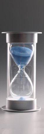 Foto de Close-up of hourglass with blue sand on gray background. Sand flowing through the bulb of sandglass. Invertible device, retro symbol of time - Imagen libre de derechos
