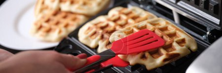 Téléchargez les photos : Close-up of waffle iron in kitchen, cooking homemade waffles. Woman preparing yummy breakfast for family - en image libre de droit
