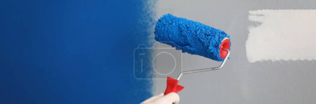 Foto de Close-up of worker with roller tool ready to paint walls, cover in blue colour. Wall with part white and blue lac. Renovation, design, redecoration concept - Imagen libre de derechos