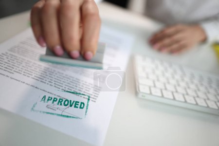 Téléchargez les photos : Closeup of a person hand stamping green approved seal on text approved document on table. Contract form and business agreement with partner - en image libre de droit