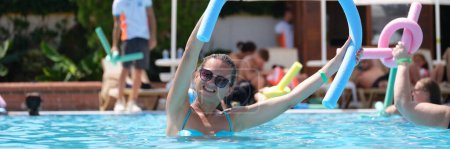Photo for Attractive smiling woman in sunglasses using swimming noodles in pool. Water aerobics and fitness in pool on vacation in hotel - Royalty Free Image