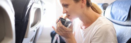 Téléchargez les photos : Woman eats juicy tasty sandwich in cabin of an airplane. In-flight catering concept - en image libre de droit