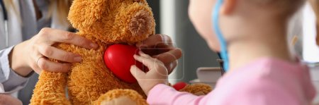 Photo for Little child girl plays with plush toy at doctor appointment. Child listens to soft toy with stethoscope and holds heart. Treatment of cardiac diseases in children - Royalty Free Image